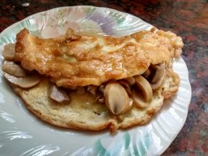 omelette de champiñones individual, color amarillo por el huevo combinado con el color de los champiñones, presentado con el relleno casi a la vista